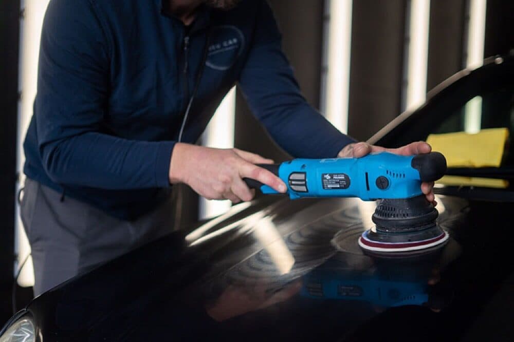 Machine polishing a black bonnet under studio lighting