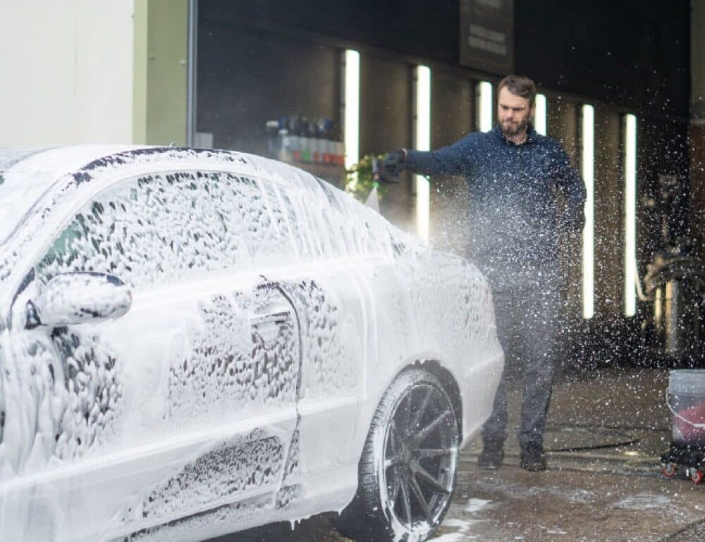 A car covered in snow foam being pressure washed