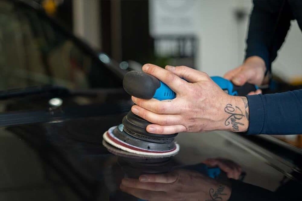 A dual action polisher working a mirror finish into dark paint